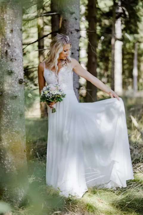 Braut Katrin mit Schleppe in der Hand und Brautstrauß im Wald - Martin Schinnerl Fotografie