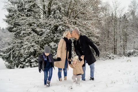 Katharina und Marcel spazieren Hand in Hand mit ihren Kindern durch den Schnee und küssen sich - Martin Schinnerl Fotografie