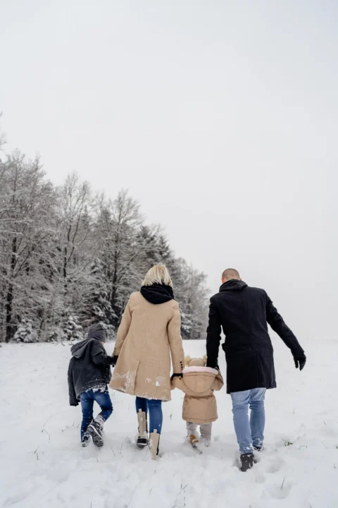 Katharina und Marcel spazieren Hand in Hand mit ihren Kindern über die verschneite Wiese am Waldrand - Martin Schinnerl Fotografie