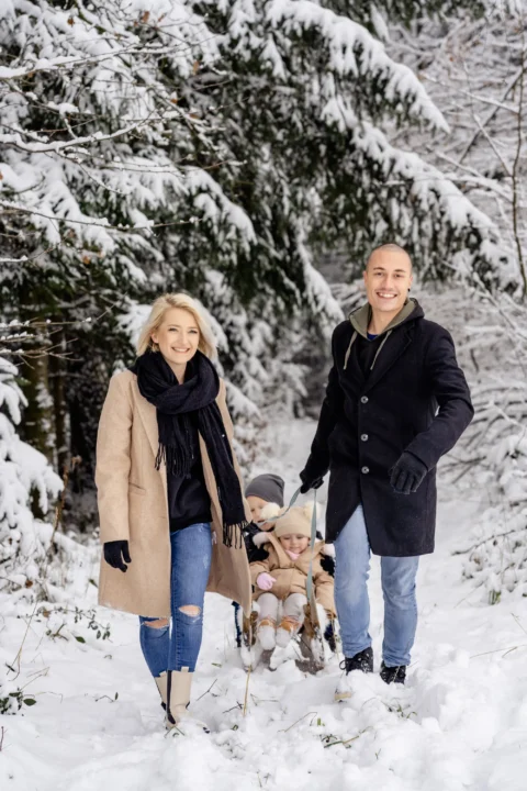 Katharina und Marcel ziehen den Schlitten mit ihren Kindern durch den schneebedeckten Winterwald - Martin Schinnerl Fotografie
