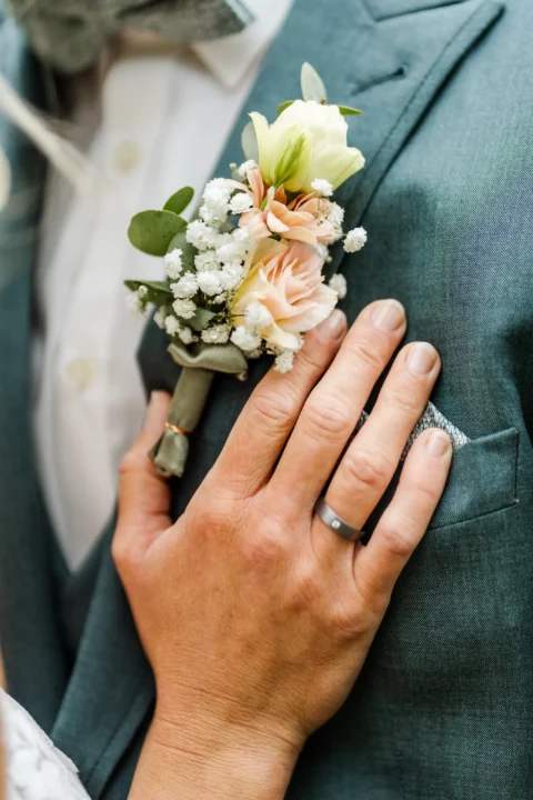 Braut legt ihre Hand mit dem Trauring neben den Blumenschmuck des Bräutigams - Martin Schinnerl Fotografie