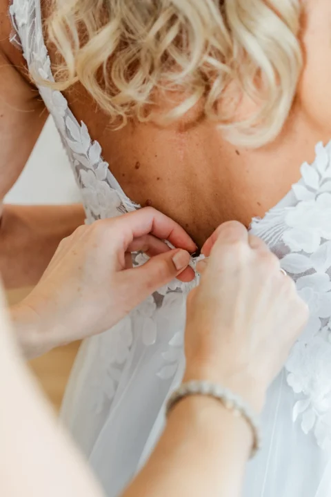 Die Braut bekommt ihr Brautkleid hinten zugemacht beim Getting Ready in Mauthausen - Martin Schinnerl Fotografie.webp