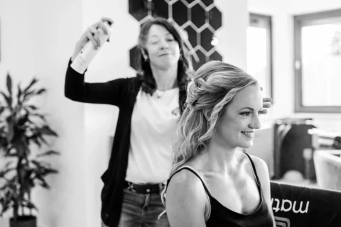 Die Braut sitzt beim Frisieren und bekommt ihre Haare gestylt beim Getting Ready zuhause in Mauthausen - Martin Schinnerl Fotografie.webp