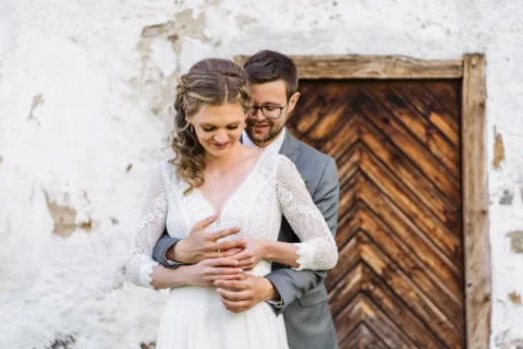 Braut und Bräutigam stecken sich gegenseitig die Trauringe an vor rustikaler Holztür im Vedahof - Martin Schinnerl Fotografie