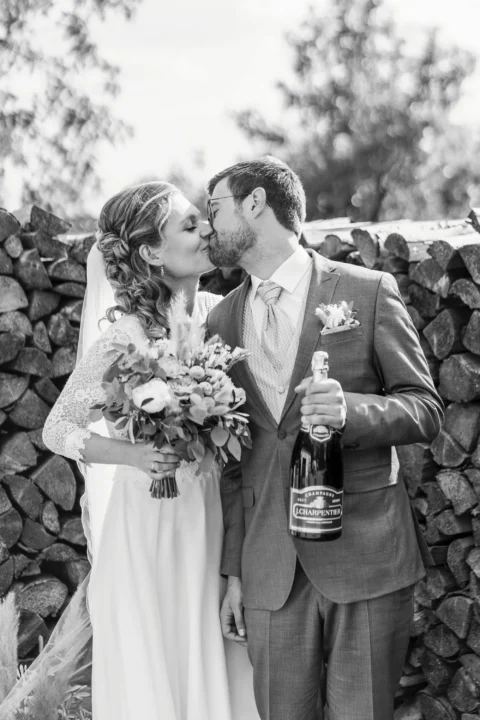 Brautpaar küsst sich neben Holzstapel mit Champagnerflasche - Martin Schinnerl Fotografie