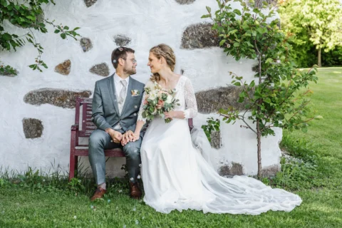 Brautpaar sitzt vor einer Steinmauer im Garten des Vedahofs bei der Hochzeit im Mai - Martin Schinnerl Fotografie