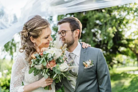 Brautpaar unter Schleier mit Brautstrauß im Garten - Martin Schinnerl Fotografie
