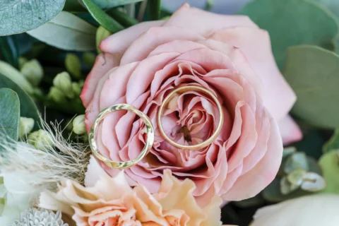 Eheringe liegen auf rosafarbener Rose im Brautstrauß - Martin Schinnerl Fotografie