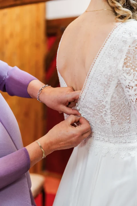Hände schließen Knöpfe am Brautkleid bei Hochzeitsvorbereitung - Martin Schinnerl Fotografie